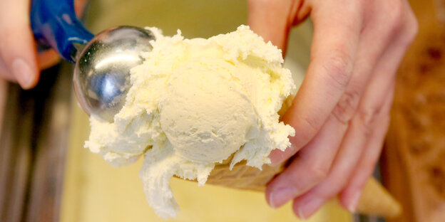 die Hände einer Eisverkäuferin, die zwei Kugeln Vanilleeis in eine Waffel tut