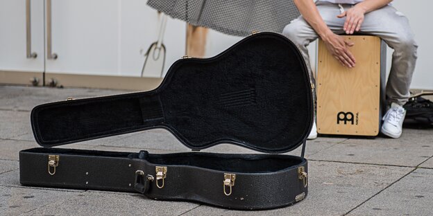 Ein Gitarrenkoffer liegt aufgeklappt vor einem Straßenmusiker Ein Gitarrenkoffer liegt aufgeklappt vor einem Straßenmusiker