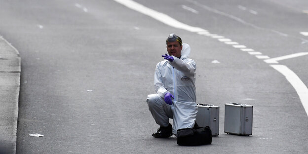Ein Mann in weißer Schutzkleidung kniet auf der Straße Ein Mann in weißer Schutzkleidung kniet auf der Straße