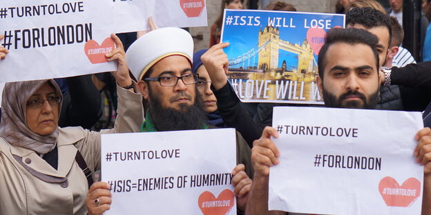 Menschen halten Zettel in die Höhe, auf denen unter anderem steht #FORLONDON und #TURNTOLOVE Menschen halten Zettel in die Höhe, auf denen unter anderem steht #FORLONDON und #TURNTOLOVE