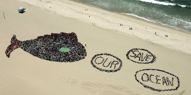 Menschen am Strand formen einen Fisch mit drei Luftblasen, in denen "Save our ocean" steht Menschen am Strand formen einen Fisch mit drei Luftblasen, in denen "Save our ocean" steht