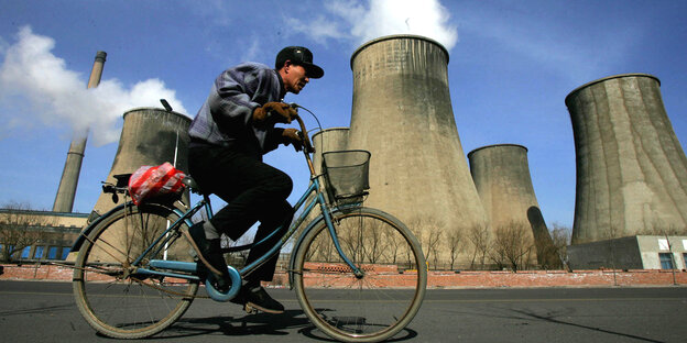 Ein Chinese fährt auf einem Fahrrad an einem Kohlekraftwerk vorbei Ein Chinese fährt auf einem Fahrrad an einem Kohlekraftwerk vorbei
