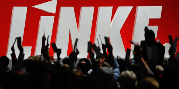 Menschen heben vor einem risigen Logo der Linkspartei Hände mit Zetteln hoch Menschen heben vor einem risigen Logo der Linkspartei Hände mit Zetteln hoch