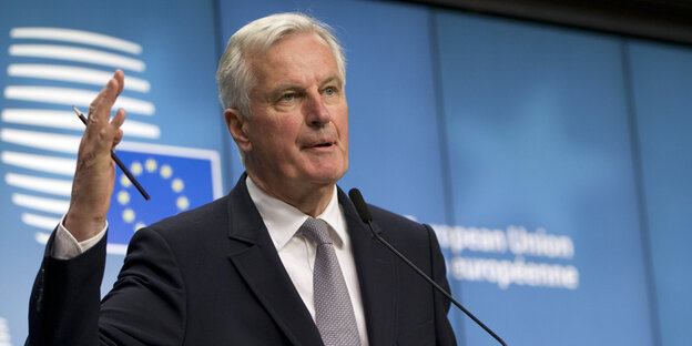 Ein Mann steht gestikulierend vor einem Banner mit dem EU-Logo Ein Mann steht gestikulierend vor einem Banner mit dem EU-Logo