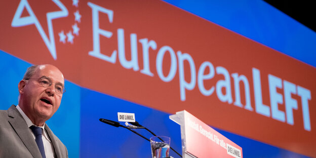 Kahler Mann mit Brille, es ist Gregor Gysi, am Rednerpult, hinter ihm die Aufschrift "European Left" Kahler Mann mit Brille, es ist Gregor Gysi, am Rednerpult, hinter ihm die Aufschrift "European Left"