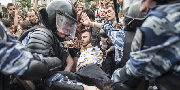 Polizisten zerren an einem Demonstranten, hinter dem andere Demonstranten stehen Polizisten zerren an einem Demonstranten, hinter dem andere Demonstranten stehen