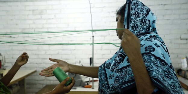 Eine Frau mit Kopftuch hält eine Schnur in der Hand. Sie arbeitet in der Textilproduktion. Eine Frau mit Kopftuch hält eine Schnur in der Hand. Sie arbeitet in der Textilproduktion.