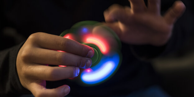 Eine Hand hält einen Fidget Spinner mit LED-Licht, die andere Hand stößt ihn an Eine Hand hält einen Fidget Spinner mit LED-Licht, die andere Hand stößt ihn an