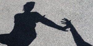 Man sieht den Schatten einer Frau, die sich gegen die Hand eines Mannes wehrt.