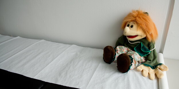 Eine Handpuppe sitzt auf der Liege einer Kinderschutzambulanz Eine Handpuppe sitzt auf der Liege einer Kinderschutzambulanz