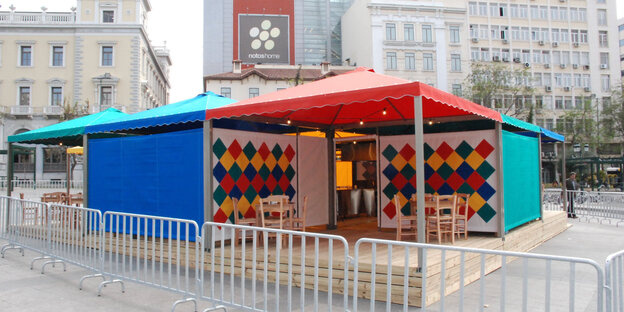 Ein kleiner bunter Pavillion in blau, türkis und rot steht auf einem Platz