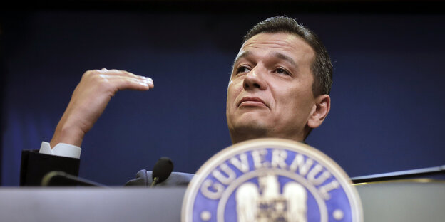 Ein Mann gestikuliert auf einem Podium mit der Hand Ein Mann gestikuliert auf einem Podium mit der Hand