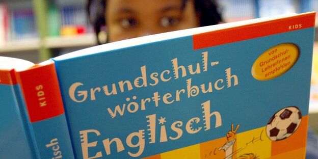 Im Vordergrund ist das Buch "Grundschulwörterbuch Englisch" zu sehen, dahinter der Kopf eines Mädchens Im Vordergrund ist das Buch "Grundschulwörterbuch Englisch" zu sehen, dahinter der Kopf eines Mädchens