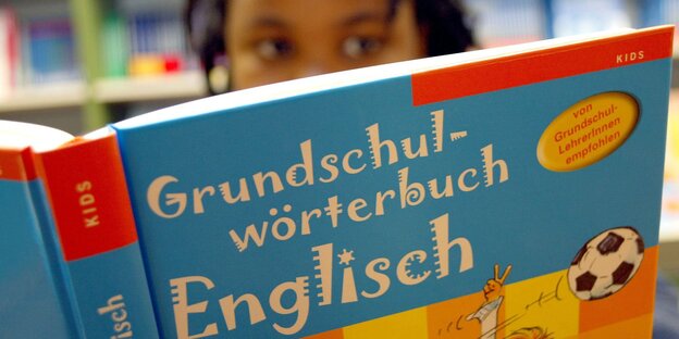 Im Vordergrund ist das Buch "Grundschulwörterbuch Englisch" zu sehen, dahinter der Kopf eines Mädchens