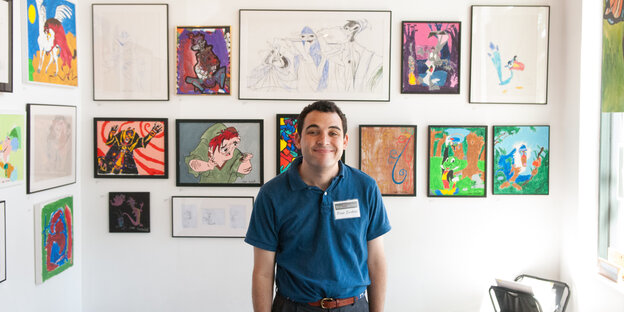 Ein junger Mann steht vor einer Wand voller Disney-Bilder und grinst Ein junger Mann steht vor einer Wand voller Disney-Bilder und grinst