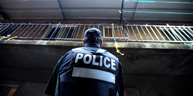 Rückenansicht eines uniformierten Polizisten, der zu einem Balkon hochschaut Rückenansicht eines uniformierten Polizisten, der zu einem Balkon hochschaut