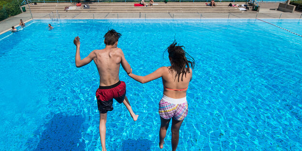Ein Junge und ein Mädchen springen in einem Freibad von einem Sprungturm ins Wasser Ein Junge und ein Mädchen springen in einem Freibad von einem Sprungturm ins Wasser