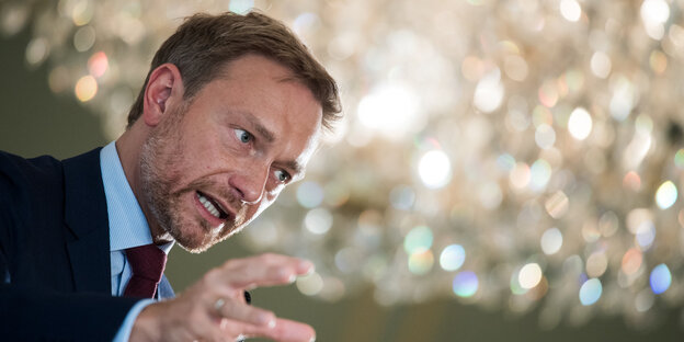 Christian Lindner steht unter einem glamurös glitzernden Kronleuchter und gestikuliert mit strenger Mine Christian Lindner steht unter einem glamurös glitzernden Kronleuchter und gestikuliert mit strenger Mine