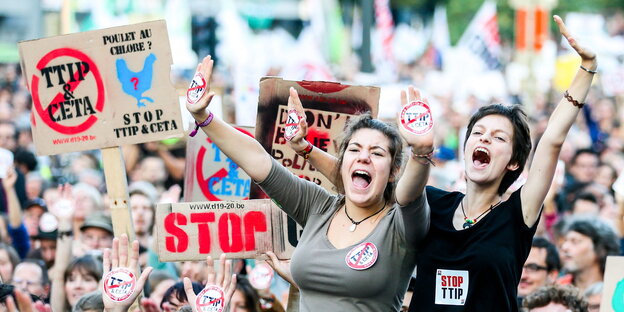 Zwei Frauen rufen und heben die Arme, hinter ihnen eine Menschenmenge. Schilder gegen Ceta und TTIP werden in die Höhe gehalten Zwei Frauen rufen und heben die Arme, hinter ihnen eine Menschenmenge. Schilder gegen Ceta und TTIP werden in die Höhe gehalten