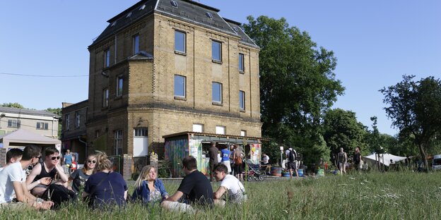 Menschen sitzen im Gras vor einem Gebäude Menschen sitzen im Gras vor einem Gebäude