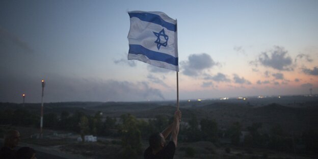 Ein Mensch hält eine Israelfahne in die Höhe Ein Mensch hält eine Israelfahne in die Höhe