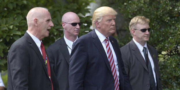 Donald Trump schreitet umringt von drei Leibwächtern durchs Bild Donald Trump schreitet umringt von drei Leibwächtern durchs Bild