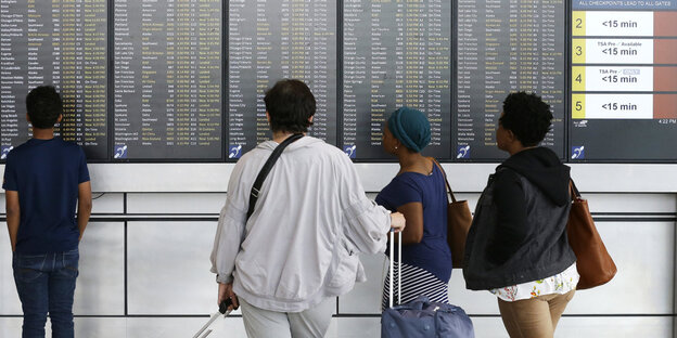 Menschen stehen vor einem Abflugplan am Flughafen Menschen stehen vor einem Abflugplan am Flughafen