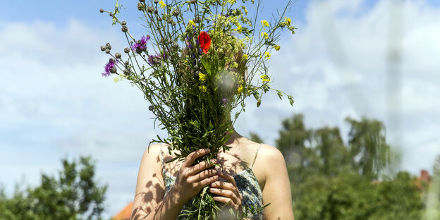 Eine Frau hält sich Blumen vors Gesicht Eine Frau hält sich Blumen vors Gesicht