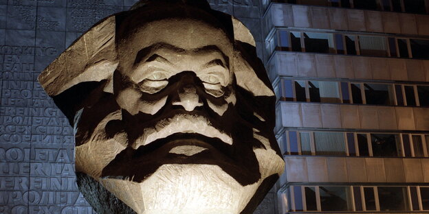 der angeleuchtete Kopf einer Karl-Marx-Statue vor einem Plattenbau der angeleuchtete Kopf einer Karl-Marx-Statue vor einem Plattenbau