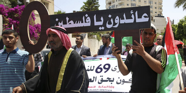 Palästinenser halten ein Schild hoch, in dem auf arabisch "wir kommen zurück Palästina" steht Palästinenser halten ein Schild hoch, in dem auf arabisch "wir kommen zurück Palästina" steht