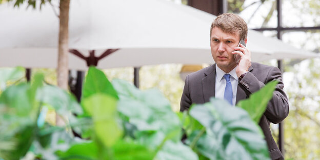 Andre Poggenburg steht mit Handy am Ohr hinter einer grünen Pflanze Andre Poggenburg steht mit Handy am Ohr hinter einer grünen Pflanze