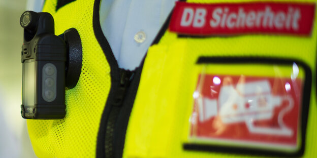 Eine Sicherheitsweste mit Bodycam, der Aufschrift "DB Sicherheit" und einer Kamerawarnung Eine Sicherheitsweste mit Bodycam, der Aufschrift "DB Sicherheit" und einer Kamerawarnung