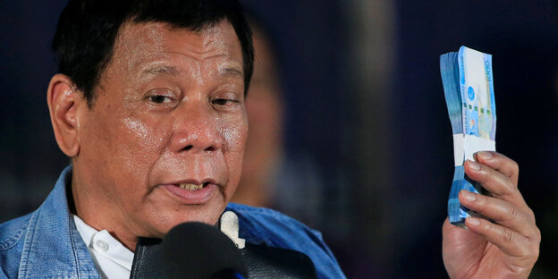 Rodrigo Duterte steht hinter einem Mikrofon und hält ein Bündel Geldscheine in die Höhe Rodrigo Duterte steht hinter einem Mikrofon und hält ein Bündel Geldscheine in die Höhe