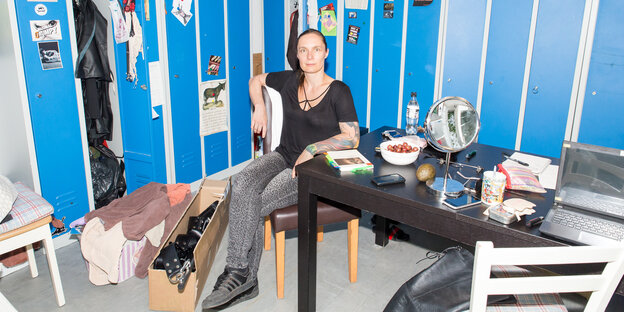 Eine dunkelhaarige Frau sitzt auf einem Stuhl. Hinter ihr sieht man Schränke Eine dunkelhaarige Frau sitzt auf einem Stuhl. Hinter ihr sieht man Schränke