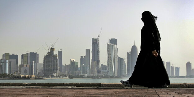 Eine verhüllte Frau spaziert vor der Skyline der Stadt Doha (Katar) Eine verhüllte Frau spaziert vor der Skyline der Stadt Doha (Katar)