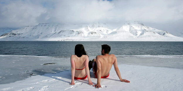 Zwei Menschen in Badekleidung sitzen im Eis und schauen auf einen Fjord Zwei Menschen in Badekleidung sitzen im Eis und schauen auf einen Fjord
