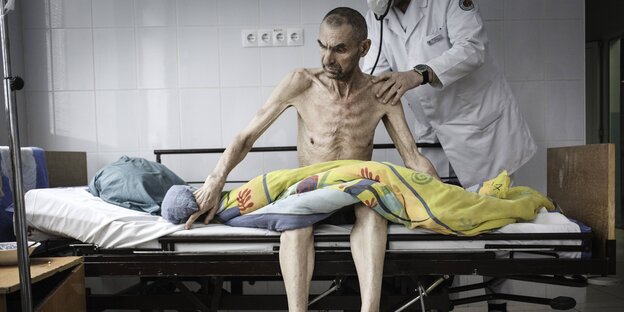 Ein Arzt untersucht einen Mann, der auf seinem Krankenhausbett sitzt Ein Arzt untersucht einen Mann, der auf seinem Krankenhausbett sitzt