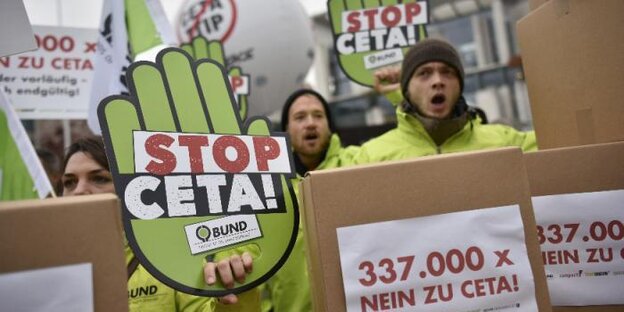 Protestierende junge Menschen neben grüner Papphand mit "Stopp Ceta"-Aufschrift Protestierende junge Menschen neben grüner Papphand mit "Stopp Ceta"-Aufschrift