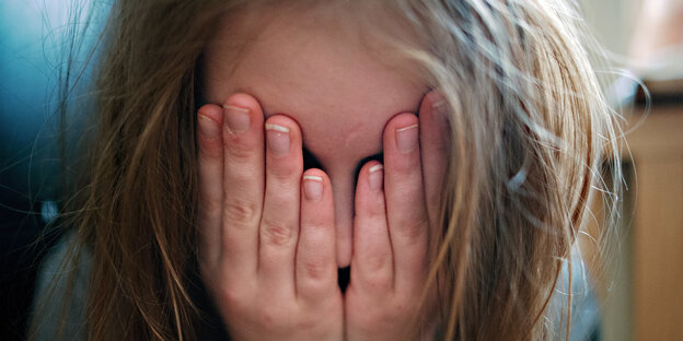 Ein Mächen mit langen blonden Haaren hält sich die Hände vors Gesicht Ein Mächen mit langen blonden Haaren hält sich die Hände vors Gesicht