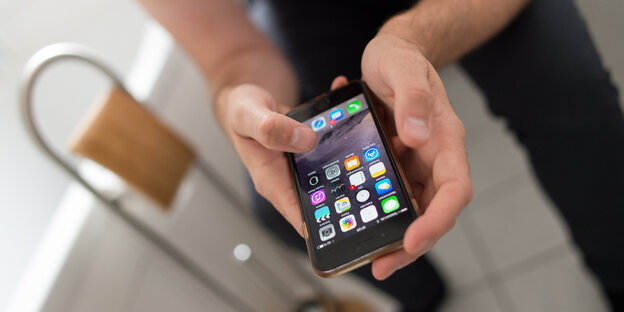 Eine Person sitzt mit dem Smartphone auf der Toilette. Eine Person sitzt mit dem Smartphone auf der Toilette.