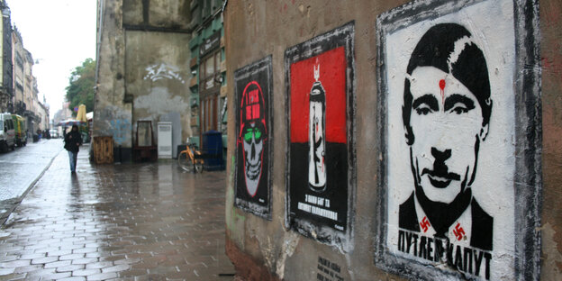Plakate an einer Hauswand. Eines zeigt Putin mit einem Hitlerbärtchen und einer Kopfschusswunde Plakate an einer Hauswand. Eines zeigt Putin mit einem Hitlerbärtchen und einer Kopfschusswunde