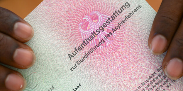 Zwei Hände auf einer Aufenthaltsgestattung eines Asylsuchenden Zwei Hände auf einer Aufenthaltsgestattung eines Asylsuchenden