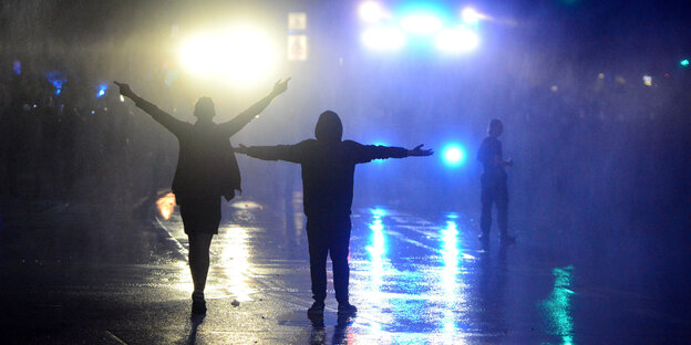Zwei DemonstrantInnen stehen auf der nächtliche Straße vor zwei Wasserwerfern Zwei DemonstrantInnen stehen auf der nächtliche Straße vor zwei Wasserwerfern