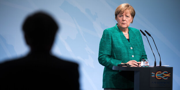 Bundeskanzlerin Angela Merkel am Rednerpult mit einem großen Schatten neben ihr Bundeskanzlerin Angela Merkel am Rednerpult mit einem großen Schatten neben ihr