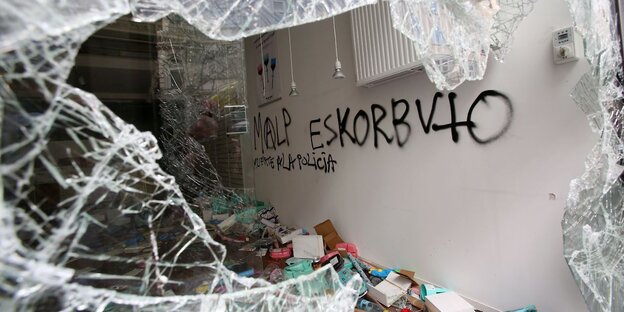 Eine eingeschlagene Scheibe, durch die man auf einer Wand einen Graffiti-Schriftzug sieht Eine eingeschlagene Scheibe, durch die man auf einer Wand einen Graffiti-Schriftzug sieht