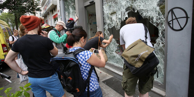 Menschen mit Smartphones fotografieren ein Loch in einer Schaufensterscheibe Menschen mit Smartphones fotografieren ein Loch in einer Schaufensterscheibe