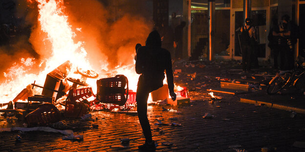 Ein Mann schießt etwas in ein loderndes Feuer in einer Straße