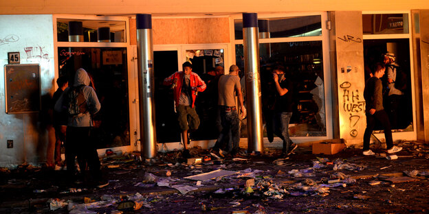 Menschen steigen durch zerbrochene Fensterscheiben eines Supermarkts