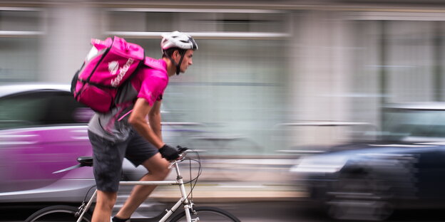 ein Radfahrer mit einer pinkfarbenen Transportrucksack für Essen auf dem Rücken ein Radfahrer mit einer pinkfarbenen Transportrucksack für Essen auf dem Rücken