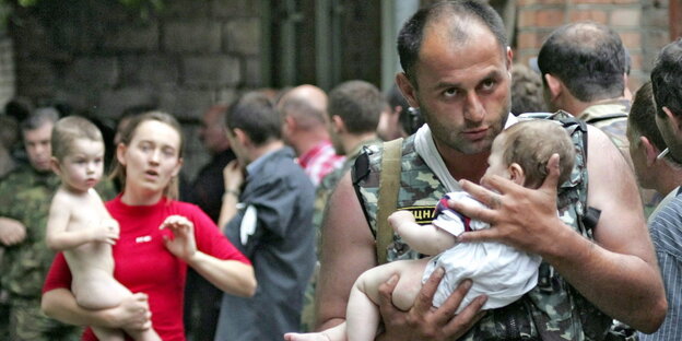 Ein Soldat und eine Frau tragen Kinder auf dem Arm, sie blicken schockiert Ein Soldat und eine Frau tragen Kinder auf dem Arm, sie blicken schockiert